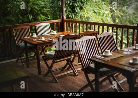 Leere Holzstühle und Tische, mit Kaffeetassen auf dem Kopf - fertig für das Frühstück, Dschungel-Regenwald im Hintergrund, Andasibe, Madagaskar, AFR Stockfoto
