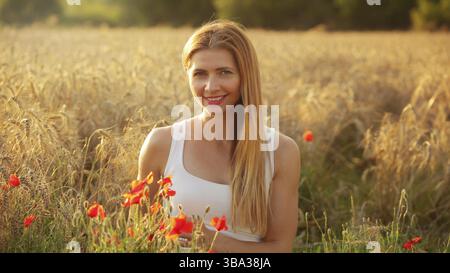 Young woman sitting in wheat field, lit by afternoon sun, few red poppies around her in foreground, Liptovsky Hradok, Slovakia, Europe Stockfoto