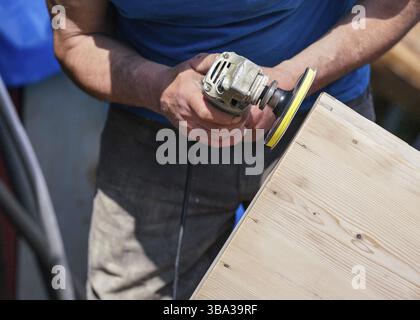 Mann poliert Holzkiste mit altem Winkelschleifer an sonnigen Tagen, Nahaufnahme an Händen ohne Handschuhe, Liptovsky Hradok, Slowakei, Europa Stockfoto