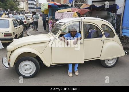 Antananarivo, Madagaskar - 24. April 2019: Unbekannter madagassischer Taxifahrer, der sich in seinem weißen Auto auf der belebten Hauptstraße ausruhte. Die Menschen sind arm, die Autos sind ruhig Stockfoto