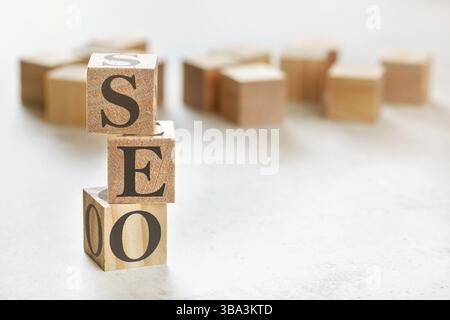 Drei Holzwürfel mit den Buchstaben SEO (bedeutet Search Engine Optimization), auf weißem Tisch, mehr im Hintergrund, Platz für Text in der rechten unteren Ecke, Lipto Stockfoto