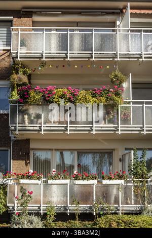 Traditionelles europäisches Wohnhaus mit Balkonen mit bunten Blumen und Blumentöpfen. Fassade eines Wohnhauses mit gepflegten Loggien und Stockfoto