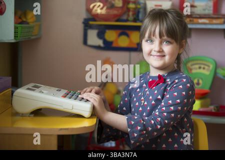 Weißrussland, die Stadt Gomil, 30. Mai 2019. Tag der offenen Tür im Kindergarten. Ein fröhliches Vorschulmädchen spielt mit einer Kasse beim Verkäufer, Europa Stockfoto