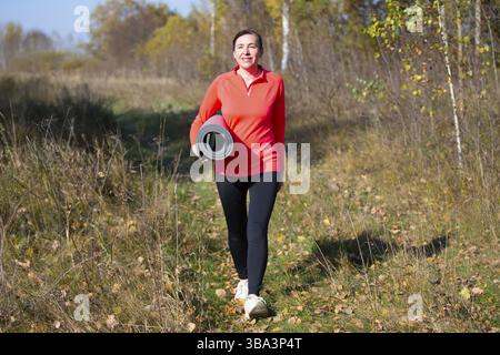 Fröhliche sportliche ältere Frau. Positive Senior Woman hält aufgerollte Trainingsmatte Gesundheit und Sport gehen Hand in Hand. Porträt eines sportlichen älteren Menschen wo Stockfoto