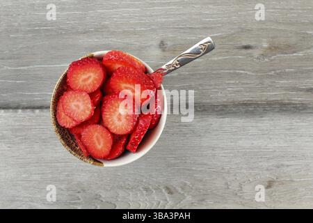 Blick auf die Tischplatte auf eine kleine Schüssel mit Himbeeren in kleinen Stücken geschnitten, mit silbernem Löffel - bereit, gesunde Snacks zu essen Stockfoto