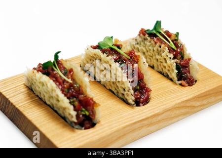 Rindersteak Tartar in Parmesankässchalen auf einem Holzbrett mit weißem Hintergrund Stockfoto