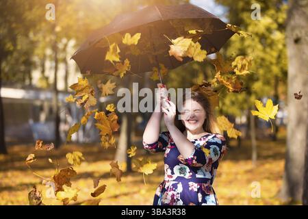 Schöne junge Frau in einem Herbstpark mit einem Regenschirm, aus dem gelbe Blätter fallen Stockfoto