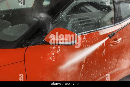 Hellrotes Auto, gewaschen in Selbstbedienungswaschanlage, Details zum Hochdruck-Wasserstrahl-Sprühen an der Vordertür, Liptovsky Mikulas, Slowakei, Europa Stockfoto