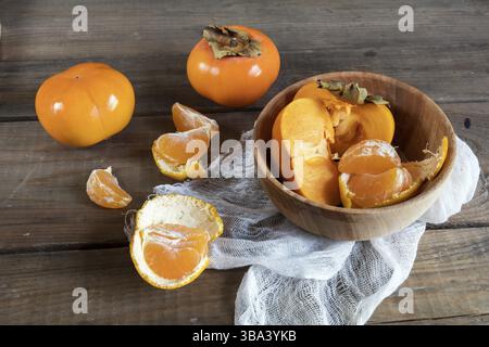 Frische Persimmonen und Mandarinenfrüchte in der Schüssel auf dunklem hölzernem Hintergrund Stockfoto