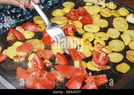 Kartoffeln und Tomaten in kleine Stücke geschnitten, gegrillt auf einem elektrischen Grill, verschwommene Hand, die Stahlgabel hält, die Räucherstücke über die heiße Oberfläche bewegt, Pribylina Stockfoto