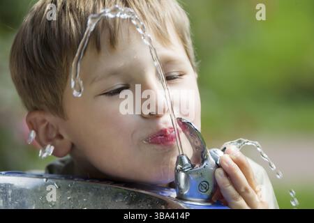 Ein Kind trinkt Wasser aus einem Brunnen. Ein Wasserstrahl und ein trinkender Mann. Durst Stockfoto