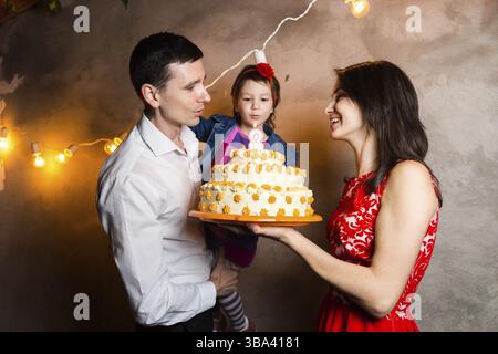 Thema Familienurlaub Kinder geburtstag und Ausblasen Kerzen am großen Kuchen. junge Familie von drei Leute stehen und halten 5 Jahre alten Tochter ich Stockfoto