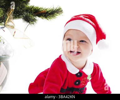 Weihnachtsmann-Baby-Mädchen im Kleid neben dem Weihnachtsbaum mit Mutterhand - mein erster Feiertag Stockfoto