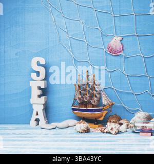 Wunderschöne Meereszusammensetzung mit Spielzeug-Segelboot, Muschel, Glasflasche und Fischernetz auf blauem Hintergrund Stockfoto