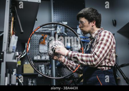 Junge kaukasische Werkstatt Reparatur Mountainbike Rad in Bike Shop Werkstatt. Fahrrad wird repariert. Pflege für Sie Räder. Mann Mechaniker arbeiten in der Garage. Stockfoto