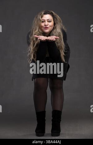 Schöne fette Frau mit langen lockigen Haaren und schwarzem Kleid, das auf ihren Armen bläst Stockfoto