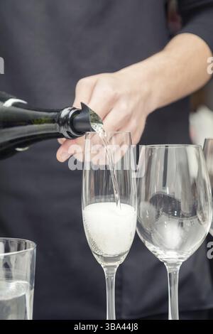 Sommelier gießt Sekt in das Weinglas. Serviertisch für eine Party oder Hochzeit vorbereitet. Weichfokus, selektiver Fokus. Getönt Stockfoto