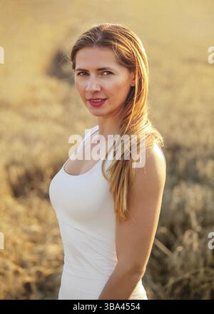 Young brunette woman in white dress, standing in wheat field lit by afternoon sun, Liptovsky Hradok, Slovakia, Europe Stockfoto
