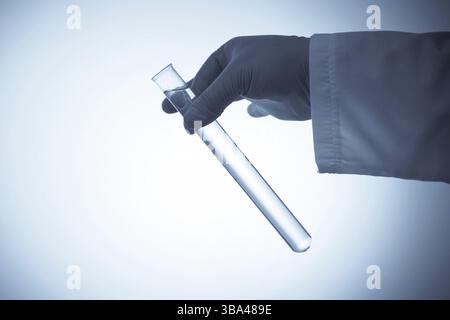 Hand in Gummihandschuh, der ein Reagenzglas mit transparenter Flüssigkeit auf blauem Hintergrund hält Stockfoto