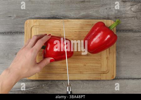 Blick auf die Tischplatte - Frau schneidet roten Paprika auf Schneidebrett mit einem Messer des Küchenchefs. Details zur Hand, Liptovsky Hradok, Slowakei, Europa Stockfoto