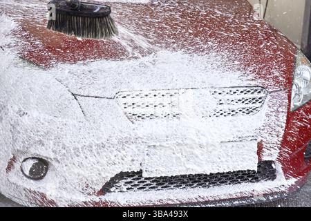 Rotes Auto gewaschen in Selbstbedienungswaschanlage, Detail auf weißem Seifenschaum, der vom Druckschlauch auf die vordere Haube sprüht, Liptovsky Mikulas, Slowakei, Europa Stockfoto