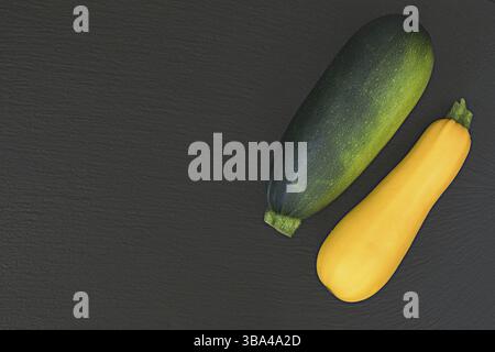 Frische grüne Zucchini und gelbe Zucchini auf schwarzer Steinoberfläche. Draufsicht, Kopierraum. Konzept für gesunde Ernährung Stockfoto