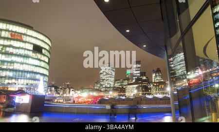 Nächtlicher Blick auf Londons Skyline vom Weihnachtsmarkt in More London, in der Nähe des Rathauses. Die Menschen schlendern entlang des Themsepfades. Stockfoto