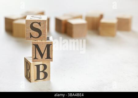 Drei Holzwürfel mit den Buchstaben SMB bedeutet kleine bis mittlere Unternehmen, auf weißem Tisch, mehr im Hintergrund, Platz für Text in der rechten unteren Ecke, Liptovsky Stockfoto