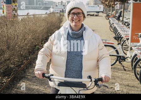 Ein Mädchen, das ein Citybike am Fahrradstand in Kopenhagen, Dänemark, ausleiht. Eine schöne Frau, die ein Fahrrad zum Mieten nimmt. Glückliche Frau, die Fahrradteile auf der Straße freigibt. Aa Stockfoto