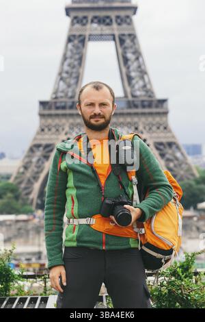 Einem jungen kaukasischen Kaukasier Mann mit einem orange Rucksack und ein Foto Kamera in den Händen steht in Frankreich, Paris vor dem Hintergrund des EIF Stockfoto