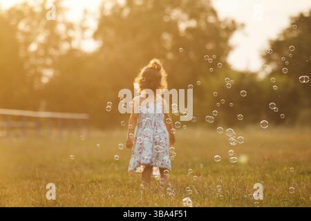Hübsches Mädchen läuft für die Bläschen im Park auf den Sonnenuntergang Stockfoto