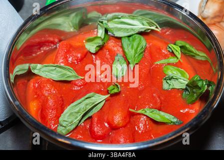 Eine Schüssel aus Edelstahl, gefüllt mit ganzen geschälten Tomaten in Sauce, garniert mit frischen Basilikumblättern, bereit zum Kochen oder für die Zubereitung von Soßen. Stockfoto