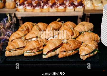 Frisch gebackene Mini-Croissants gefüllt mit Käse, Blattgemüse und Feinkostfleisch, serviert als elegantes Fingerfood für Catering-Veranstaltungen. Stockfoto