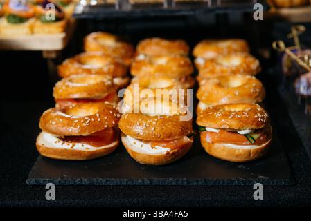Nahaufnahme von Gourmet-Mini-Bagels gefüllt mit Räucherlachs, Frischkäse und Gurken, auf einem schwarzen Serviertablett angeordnet. Stockfoto