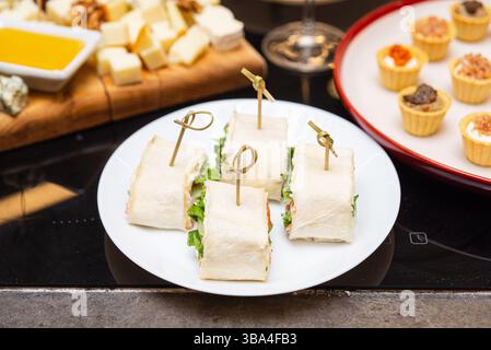 Kleine Tortilla-Wrap-Bissen gefüllt mit Salat und Fleisch, gesichert mit Picks, serviert auf einem weißen Teller als Party-Snacks. Stockfoto