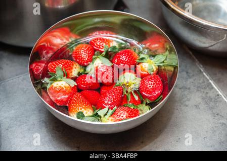 Hellrote Erdbeeren, die in einer Edelstahlschale mit Wasser einweichen, frisches Obst für den Nachtisch oder gesunde Snacks zubereiten. Stockfoto