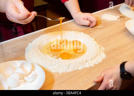 Zerrissene Eier in einer Wanne Mehl auf einer Holzoberfläche, die von Hand in frischen Teig gemischt werden können. Stockfoto