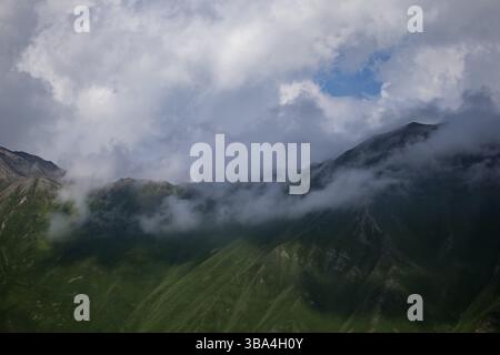 Dunkle atmosphärische surreale Landschaft mit einem dunklen felsigen Berggipfel in niedrigen Wolken in einem grau bewölkten Himmel. Eine graue, niedrige Wolke auf einem hohen Gipfel. Hoher schwarzer roc Stockfoto