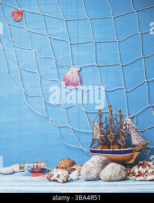 Wunderschöne Meereszusammensetzung mit Spielzeug-Segelboot, Muschel, Glasflasche und Fischernetz auf blauem Hintergrund Stockfoto
