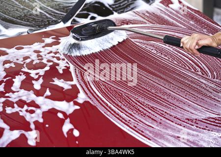 Rotes Auto gewaschen in Selbstbedienungs-Waschanlage auf Bürste, die über die vordere Motorhaube bewegt wird, mit weißen Seifenstrichen, Liptovsky Mikulas, Slowakei, Europa Stockfoto