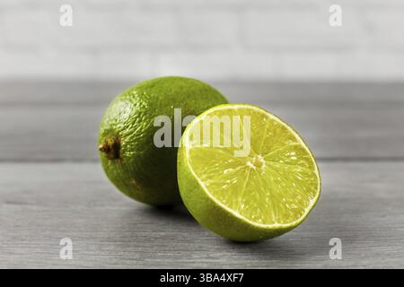 Ganze Limette und eine andere, die in zwei Hälften geschnitten wurde, auf einem grauen Holztisch Stockfoto
