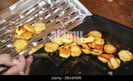 Kartoffeln in kleine Kreise geschnitten, mit Gewürzen gewürzt, auf Elektrogrill gegrillt - Frau hält Spachtel, indem sie gekochte Speisen auf Aluminiumfolie tra verschiebt Stockfoto