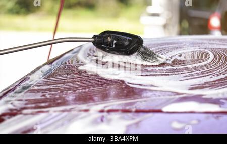 Pinsel hinterlässt Striche in weißem Shampoo und Schaum auf dem Dach des roten Autos, gewaschen in Selbstbedienungswaschanlage, Liptovsky Mikulas, Slowakei, Europa Stockfoto