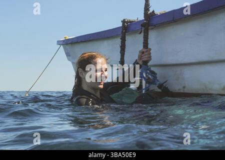 Junge Frau in Neopren, lächelnd, Maske schon entfernt, nach ihrem Tauchgang vom Meer aus zum Boot, Anakao, Madagaskar, Afrika Stockfoto