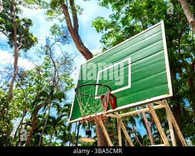 Blick aus dem unteren Winkel des Basketballkörpers aus alter grüner Holzplatte mit Netz umgeben von Palmen in der Nähe des Strandes am blauen Sommerhimmel Stockfoto