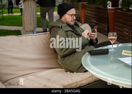 Odessa, Ukraine - 21. April 2025: Ein bärtiger Mann in Brille mit einem Telefon in den Händen. Stockfoto