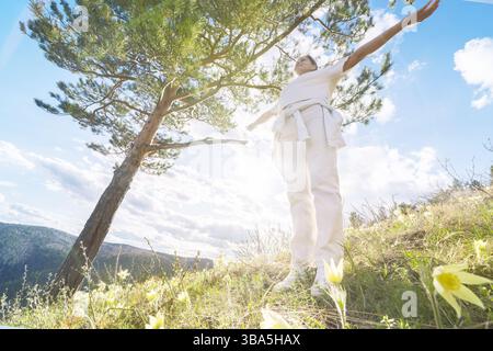 Eine Frau steht auf einem Feld voller lebendiger Blumen und genießt die sanfte Wärme der Sonne an einem hellen Frühlingstag. Umgeben von grünen Bergen und Stockfoto
