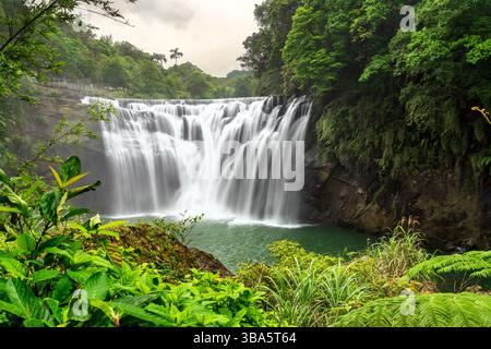 Der Shifen Wasserfall im Pingxi District in New Taipei, Taiwan, stürzt sich in einen türkisfarbenen Pool inmitten von dichtem Grün und bietet eine malerische und ruhige natürliche Attraktion, die oft als Little Niagara von Taiwan bezeichnet wird Stockfoto