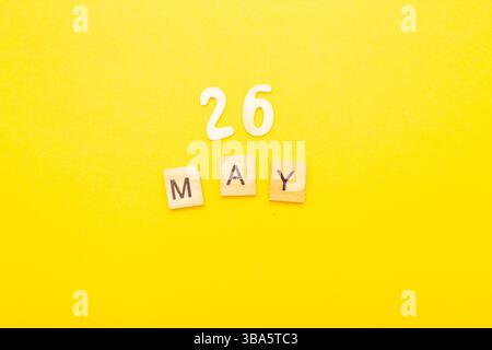 Draufsicht des Wortes 26. Mai Kalenderdatum aus Holzwürfeln auf gelbem Hintergrund. Kalender- und Frühjahrskonzept. Stockfoto