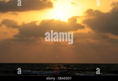 Goldener Sonnenuntergangshimmel mit dramatischen dunklen Wolken und Sonnenstrahlen, die durch eine atemberaubende Naturszene strömen. Stockfoto